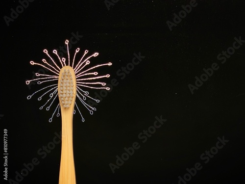 Bamboo toothbrush on black. Dandelion flower drawn on holographic scratch paper. No plastic concept, zero waste.