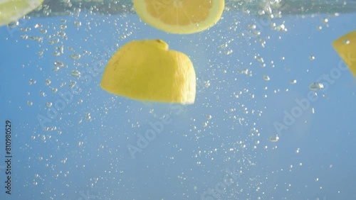 Super slow motion video of lemon falling into water with a splash. Blue background.