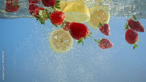 Close-up Strawberries and lemons dip into the water, creating a vibrant, refreshing splash.Blue background