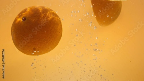 Super slow motion video of orange slices falling into water with a splash. Yellow background.