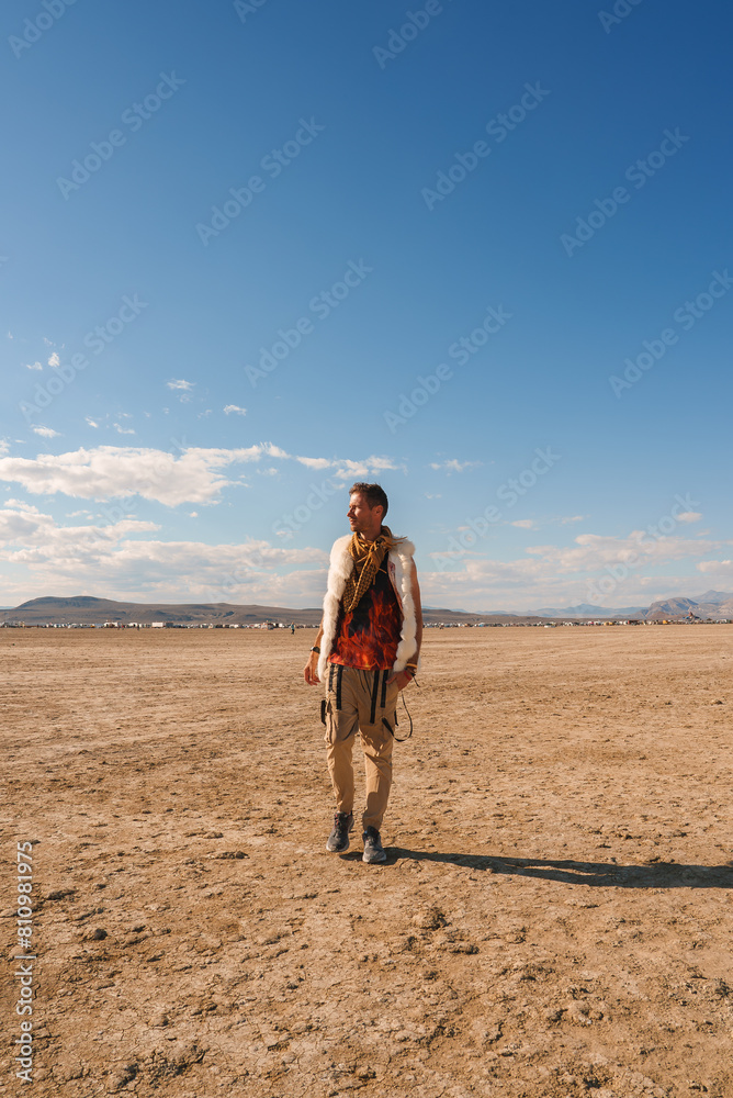 Individual in eclectic outfit stands alone in vast desert landscape under clear blue sky. Mountains in distance convey sense of isolation and solitude. Individual in eclectic outfit stands alone in vast desert landscape under clear blue sky. Mountains in distance convey sense of isolation and solitude.