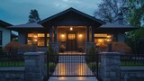 Late evening at a craftsman house in slate grey, porch lights creating a soft glow by the rod gate.