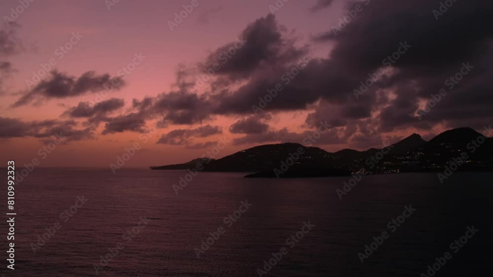 Red sunset sky is reflected in sea, and dark cloudscape replicating silhouette of Sint Maarten hills strewn with city lights of evening Phillipsburg Red sunset sky is reflected in sea, and dark cloudscape replicating silhouette of Sint Maarten hills strewn with city lights of evening Phillipsburg
