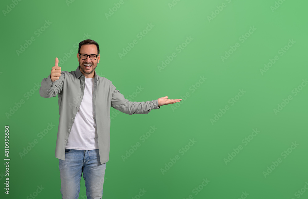 Salesman laughing and demonstrating product on palm and showing thumbs up sign on green background Salesman laughing and demonstrating product on palm and showing thumbs up sign on green background