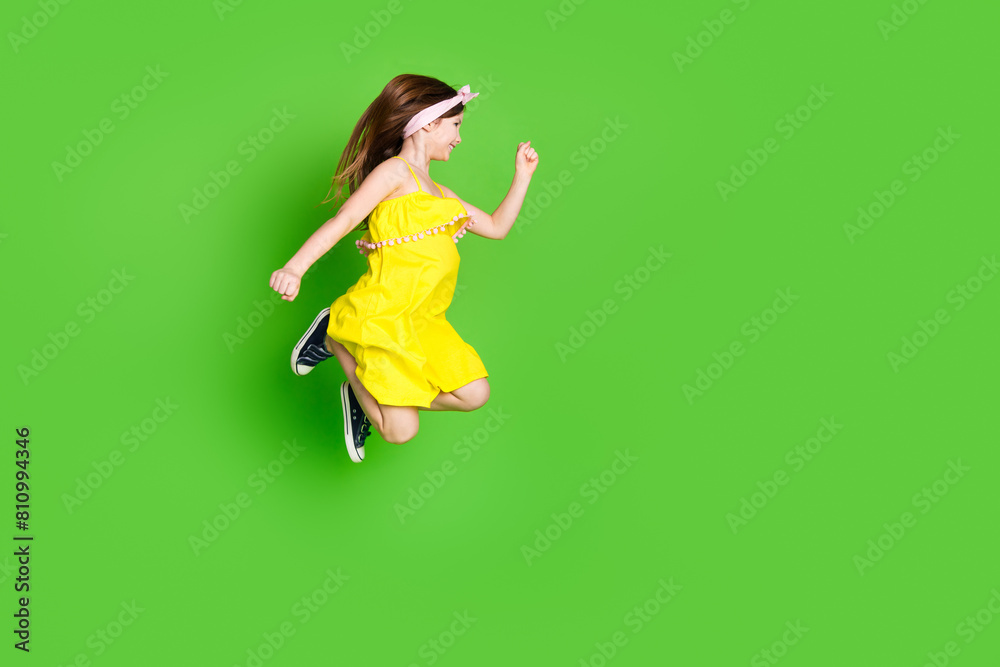Full length photo of adorable lovely small girl wear pin up dress jumping high running empty space isolated green color background Full length photo of adorable lovely small girl wear pin up dress jumping high running empty space isolated green color background