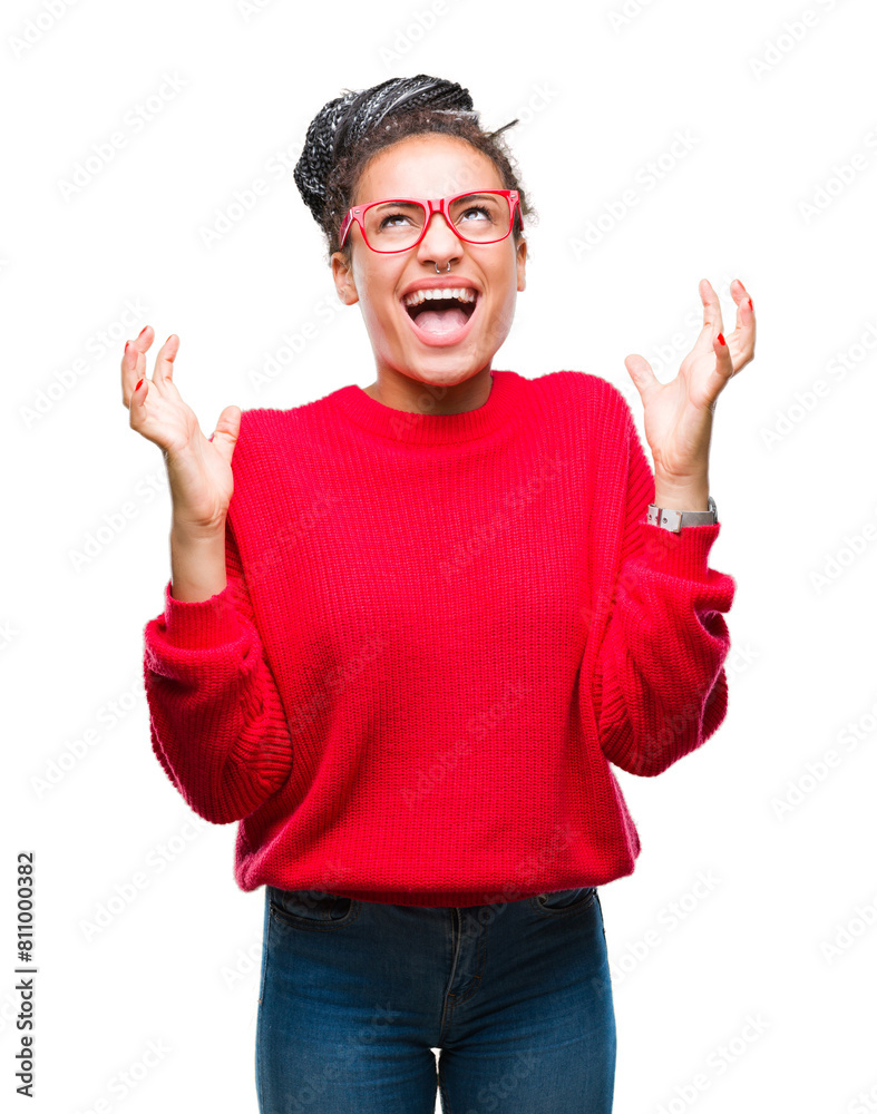 Naklejka premium Young braided hair african american girl wearing sweater and glasses over isolated background celebrating mad and crazy for success with arms raised and closed eyes screaming excited. Winner concept