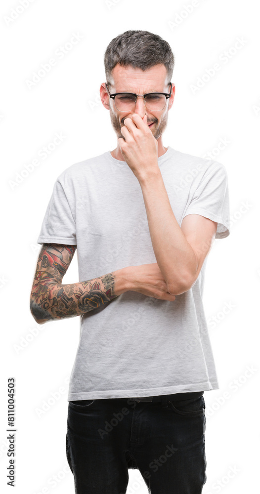 Young tattooed adult man smelling something stinky and disgusting, intolerable smell, holding breath with fingers on nose. Bad smells concept. Young tattooed adult man smelling something stinky and disgusting, intolerable smell, holding breath with fingers on nose. Bad smells concept.