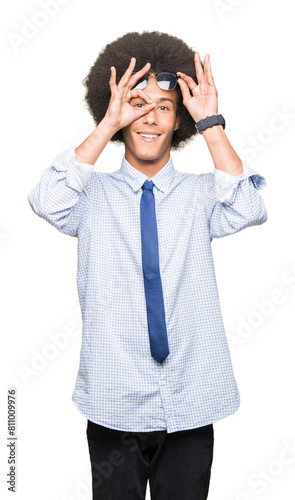 Young african american business man with afro hair wearing sunglasses doing ok gesture with hand smiling, eye looking through fingers with happy face.