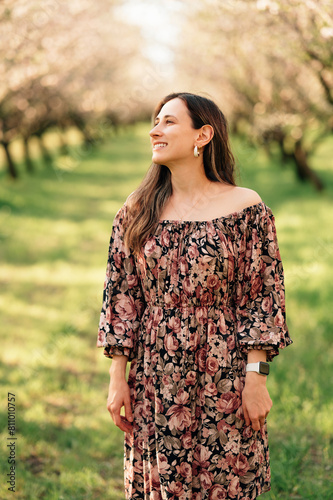 Vertical outdoors portrait of a smiling woman wearing dress in almond orchard.