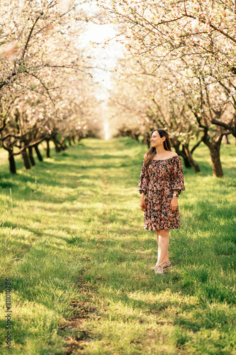 Vertical outdoors shot of a woman wearing dress walking in a almond orchard.