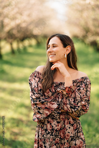 Vertical outdoors portrait of a smiling woman wearing dress in almond orchard.