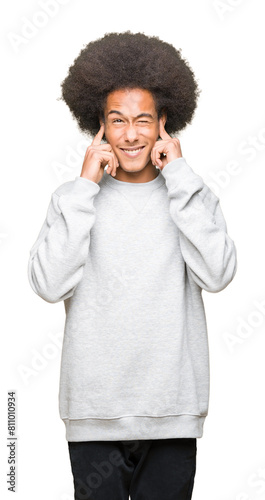 Young african american man with afro hair wearing sporty sweatshirt covering ears with fingers with annoyed expression for the noise of loud music. Deaf concept.