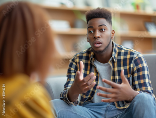 A casually dressed young African American millennial guy seeks therapy with a female psychologist in a spacious office, emotionally sharing his feelings and making gestures.
