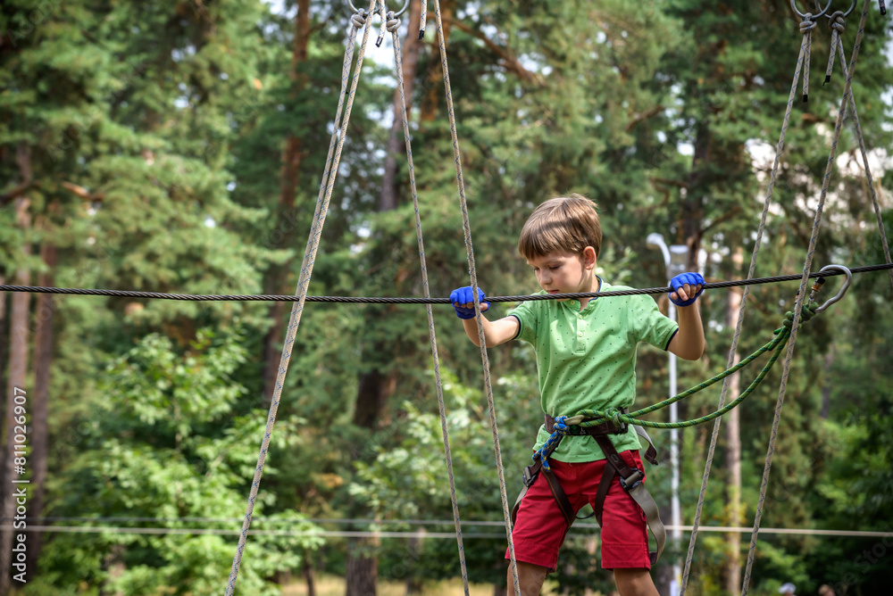 Strong excited young boy playing outdoors in rope park. Caucasian child dressed in casual clothes and sneakers at warm sunny day. Active leisure time with children concept Strong excited young boy playing outdoors in rope park. Caucasian child dressed in casual clothes and sneakers at warm sunny day. Active leisure time with children concept
