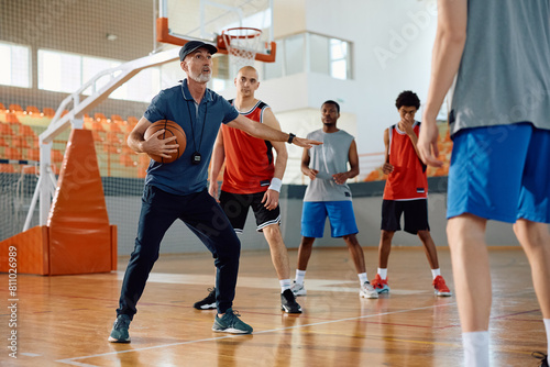 Basketball coach having sports training with group of players in school gymnasium.