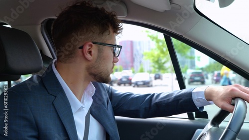 Young man in glasses and suit driving into a parking near a shopping center in the city. Transport, business and people concept. Real time © Nataliya