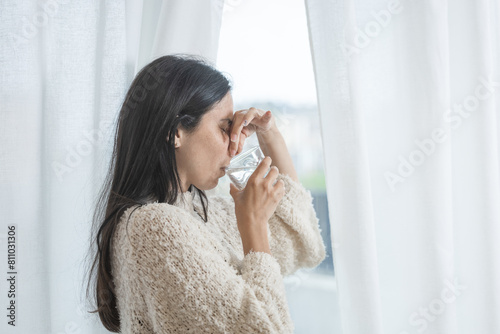 Overwhelmed woman suffering from pain and taking medicine that tastes bad in a glass of water.
