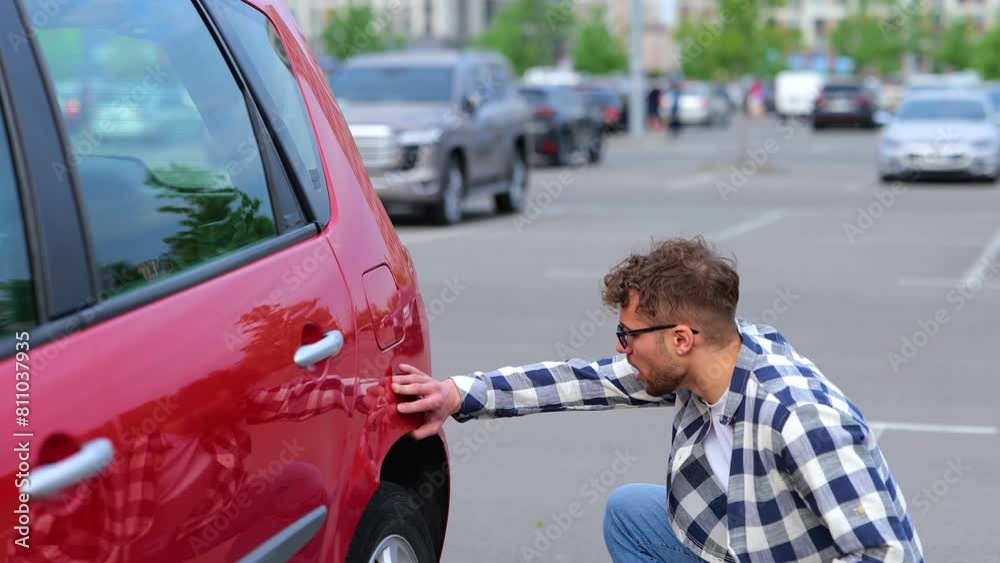 Upset young man sitting near the car on the parking, a tire puncture, a flat car wheel. Transportation, broken car, travel concept. Real time Upset young man sitting near the car on the parking, a tire puncture, a flat car wheel. Transportation, broken car, travel concept. Real time