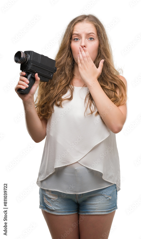 Young blonde woman holding super 8 video camera cover mouth with hand shocked with shame for mistake, expression of fear, scared in silence, secret concept Young blonde woman holding super 8 video camera cover mouth with hand shocked with shame for mistake, expression of fear, scared in silence, secret concept