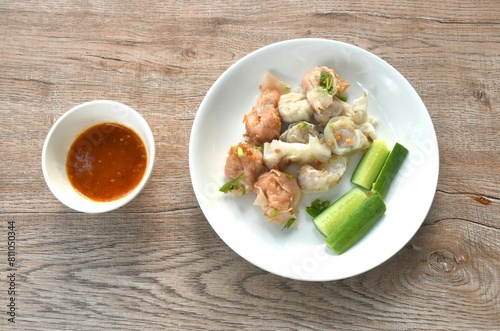 steamed fish and shrimp dumpling topping crispy  fried chop garlic with cucumber on plate dipping spicy and sour sauce cup