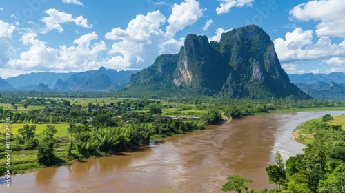 an aerial view showcasing a flowing river amidst lush tropical rainforest, flanked by verdant green mountains under a vast sky, presenting a serene landscape panorama.