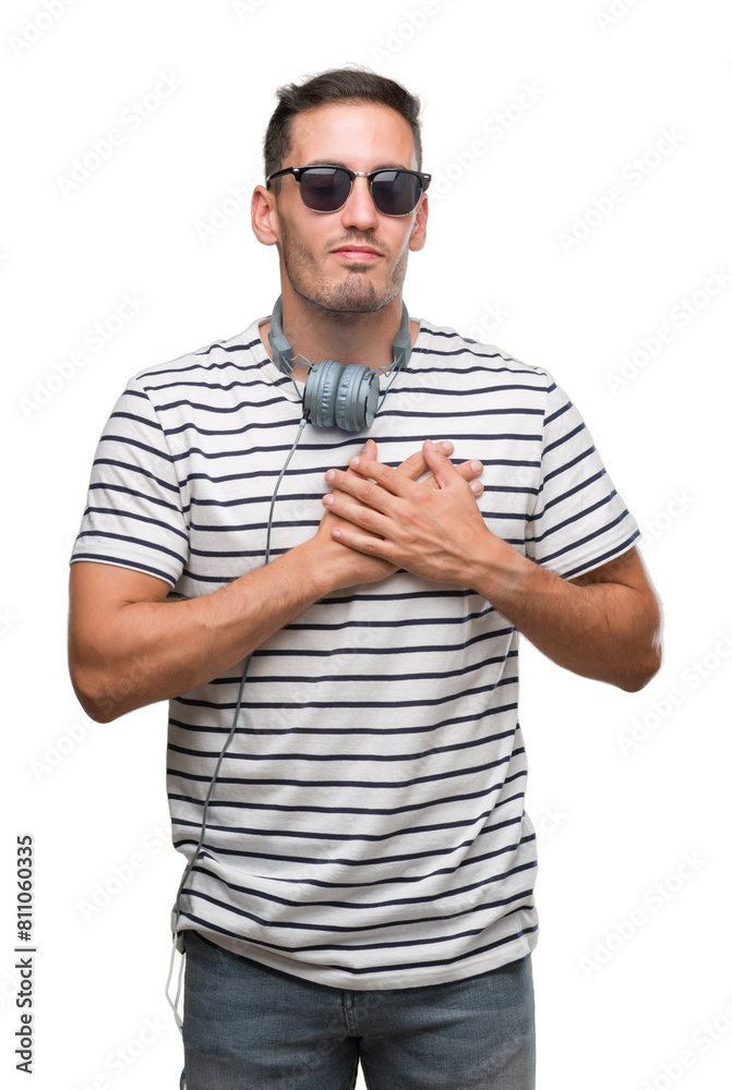 Handsome young man wearing headphones smiling with hands on chest with closed eyes and grateful gesture on face. Health concept. Handsome young man wearing headphones smiling with hands on chest with closed eyes and grateful gesture on face. Health concept.