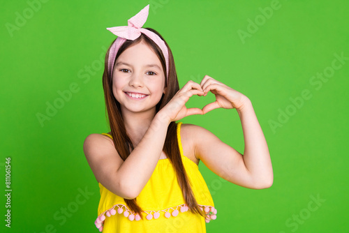 Photo of charming cute small girl wear yellow dress showing arms heart empty space isolated green color background