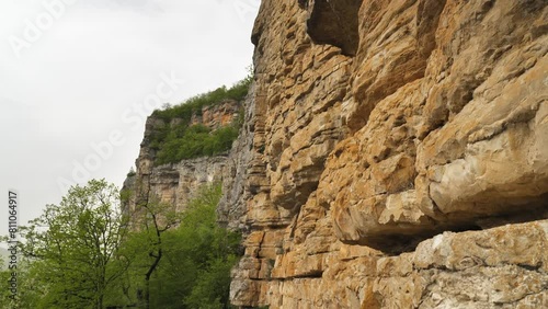 The rugged beauty of the cliffs with visible layers of sedimentary rocks. The rocks are predominantly brown and beige in colour. The path at the base of the cliff is a popular hiking spot photo