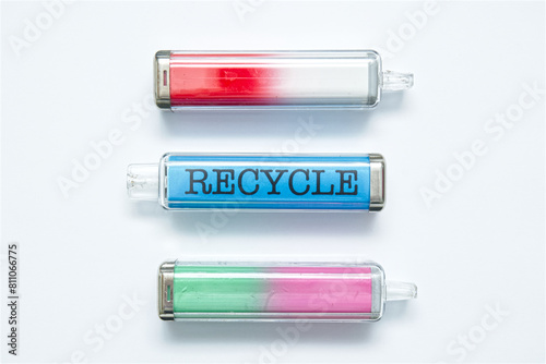 Discarded single use electronic cigarette vapes. The middle one spelling the word RECYCLE. Isolated on a white paper background.