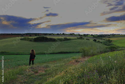 FIELD WITH TREES AND FLOWERS AT SUNSET AND A WOMAN OBSERVING THE LANDSCAPE © PATRICIA