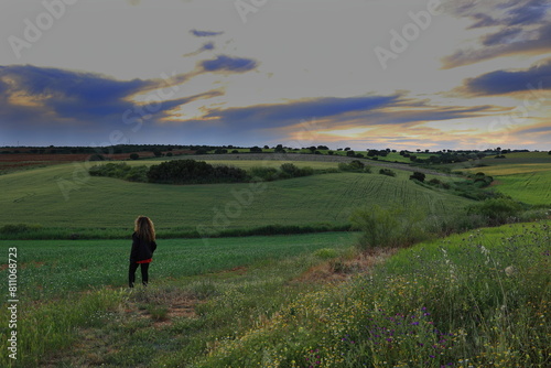 FIELD WITH TREES AND FLOWERS AT SUNSET AND A WOMAN OBSERVING THE LANDSCAPE