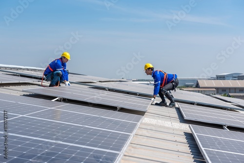 Two solar panel technicians in hard hats and safety gear install solar panels on a commercial building