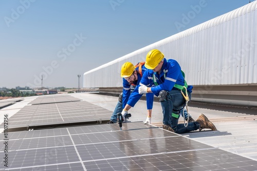 Two solar panel installation workers wearing safety gear are installing solar panels on a commercial building's roof.