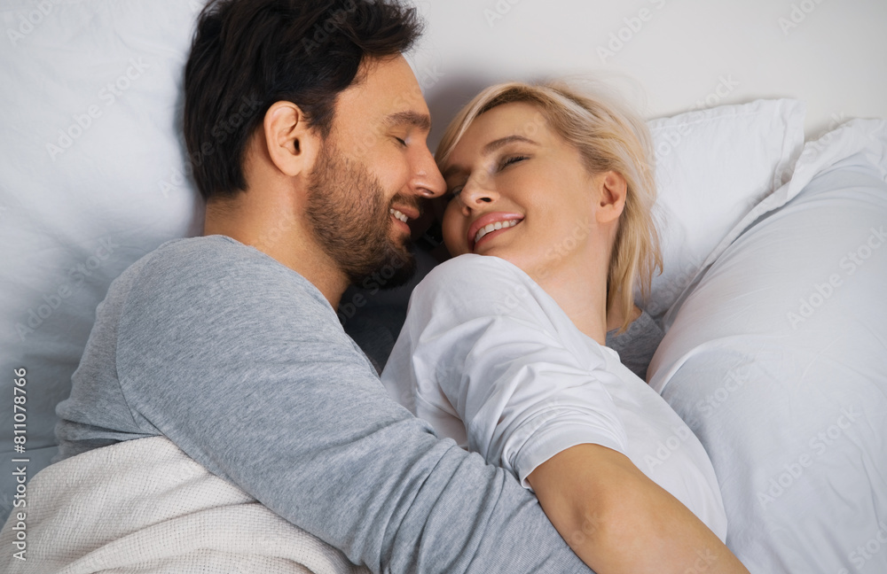 Image of young playful married couple looking at each other, lay on home bed. Blond attractive woman, brunette bearded man in love, happy family, flirting, planning pregnancy concept. Image of young playful married couple looking at each other, lay on home bed. Blond attractive woman, brunette bearded man in love, happy family, flirting, planning pregnancy concept.