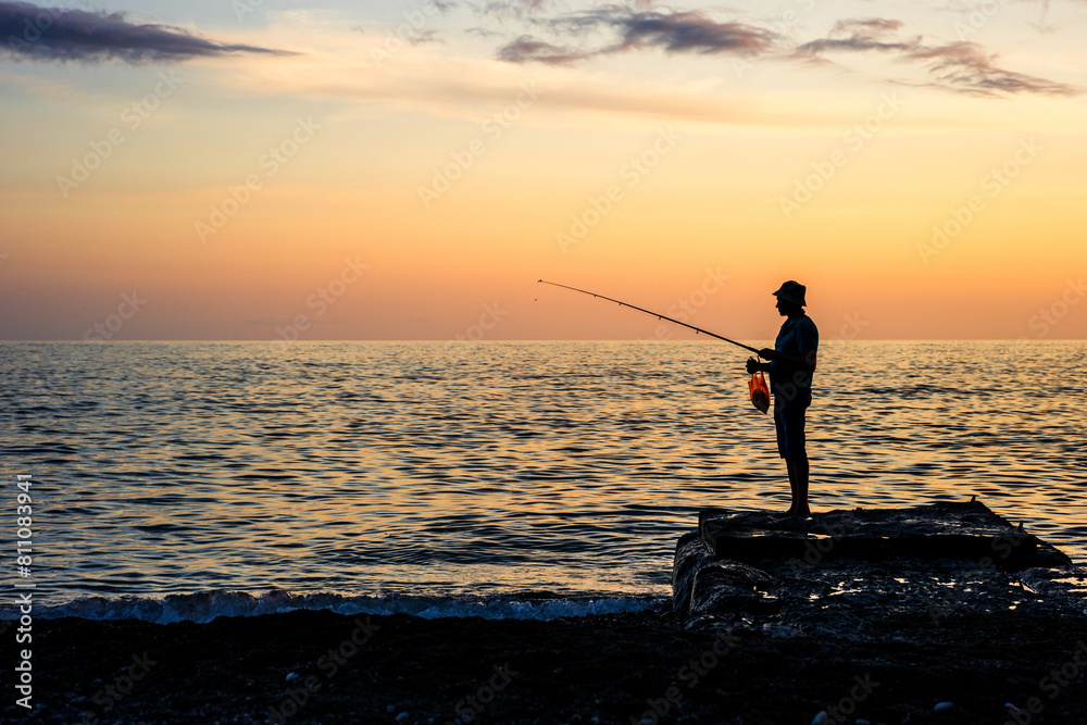 the silhouette of a fisherman in a hat with a fishing rod against the sunset background