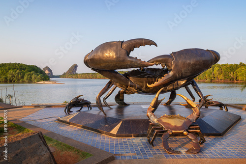 The Mud Crabs Sculpture by a scenic river landscape in Krabi Town, Thailand on a sunny day. Khao Kanab Nam, the two famous twin limestone mountains, and mangrove forests are in the background.