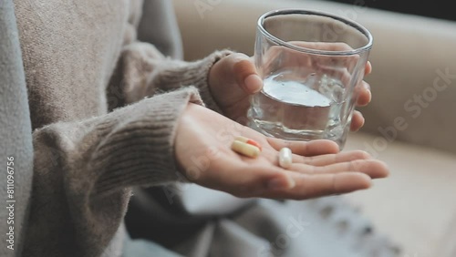 Unhealthy sick woman suffers from insomnia or headache, takes sleeping pill while sitting in bed with glass of water, depressed girl holds antidepressant meds, painkiller for menstrual pain, close up photo