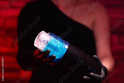 Sex toys for men. A male automatic telescopic masturbator in the hands of a girl in black latex gloves and a black dress on a red background. Male massager. Sex shop Adult store, toys for two photo