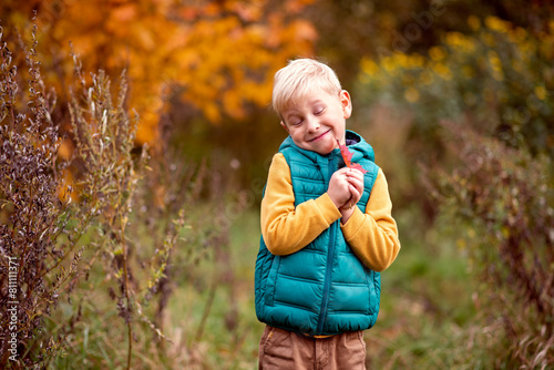 Cute little blond boy in the autumn forest. Happy child on the street.