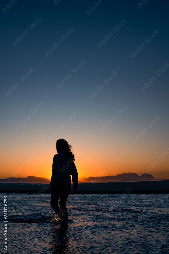 silhouette of a woman watching the sunset while walking in the ocean