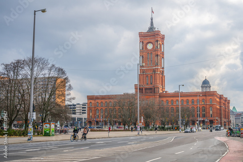 The iconic Red City Hall in Berlin stands out against a cloudy sky as evening falls, with city life bustling in the foreground. Berlin, Germany