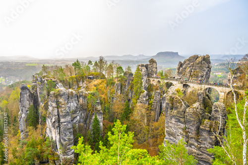 The Bastei Bridge stands tall among majestic sandstone rock formations with visitors enjoying the scenic view at sunset. Kurort Rathen, Saxon Switzerland, Germany