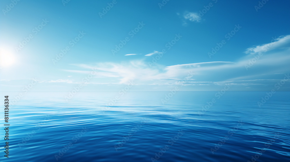 Calm ocean water under a clear blue sky with soft, wispy clouds and bright sunlight.