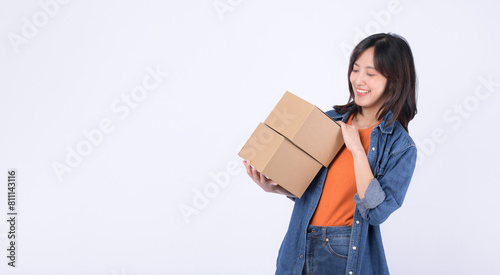 young asian woman wearing orange t-shirt and denim shirt holding parcel box isolated on white studio background, Delivery courier and shipping service concept. © Jirawatfoto