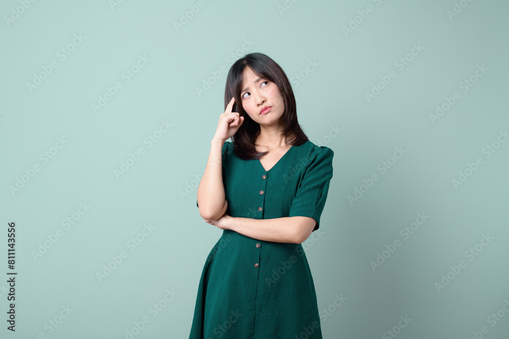An Asian woman with green suit is pondering against a green background.
