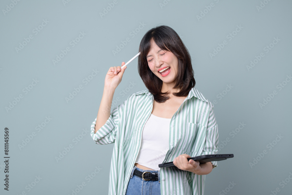 Fototapeta premium Portrait of young asian woman, teacher or student with digital tablet and pencil, writing, taking notes, doing her homework, standing over green background