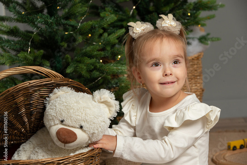 A funny little girl takes a fluffy teddy bear out of the basket in the Christmas room. photo