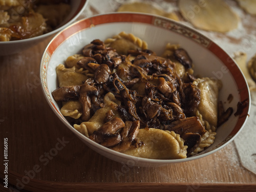 Horizontal close-up of a dish with Ukrainian varenyky, dumplings akin to Italian ravioli, with mushroom sauce on top. Some raw dough in the background.