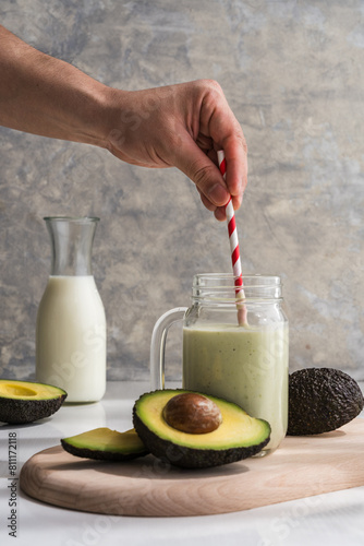 hand stirring an avocado smoothie with a straw