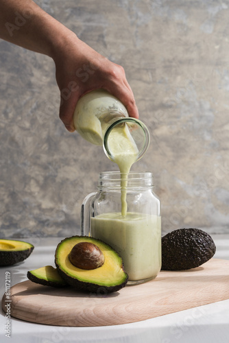 hand pouring an avocado smoothie in a glass pitcher using a glass bottle
